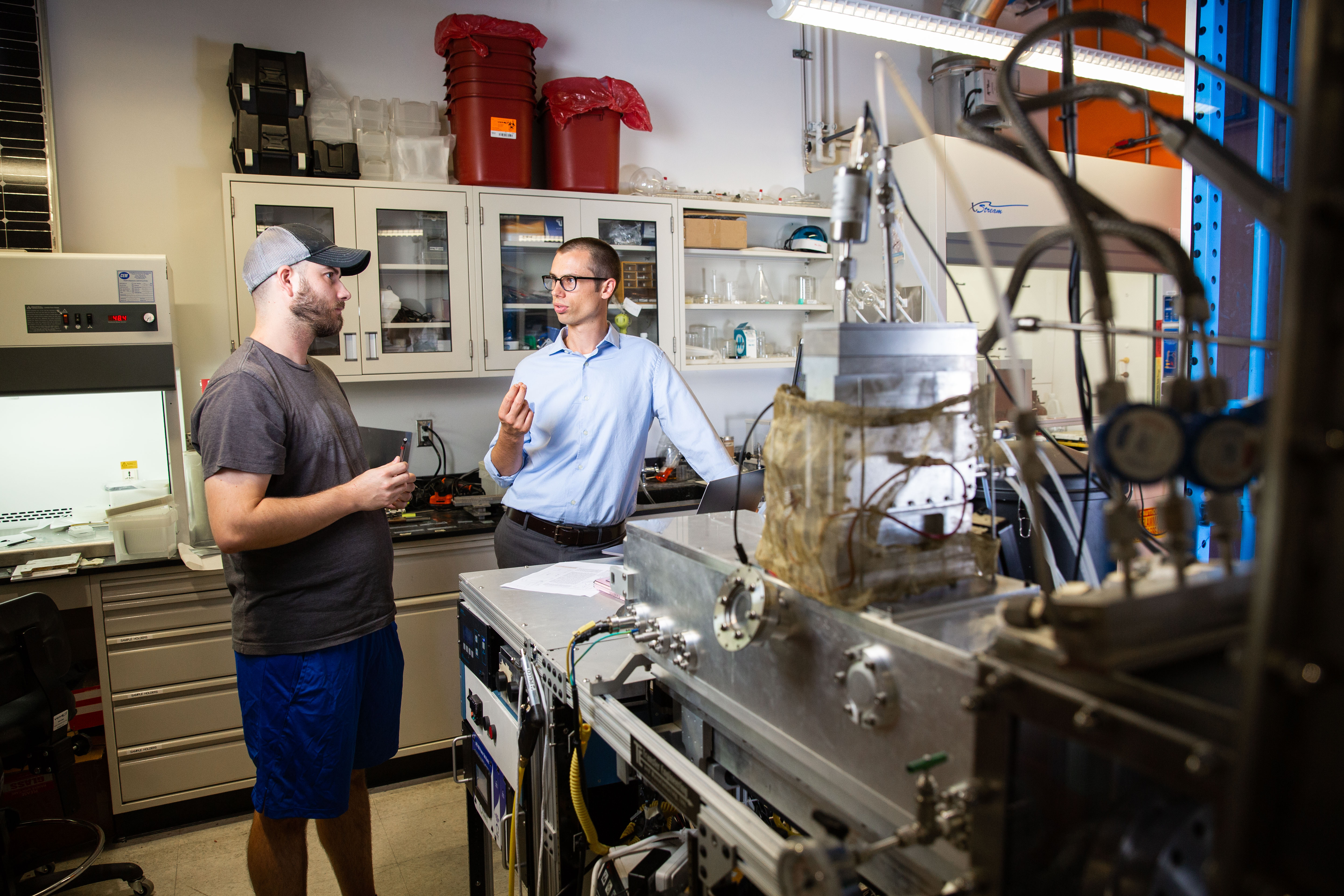 Arizona State University Assistant Professor, Zachary Holman (right), talks with Doctoral Student, Peter Firth, next to a prototype of a nano-particle deposition tool. Holman was awarded a Moore Inventor Fellowship to further develop a technique that can add beneficial properties to ordinary surfaces through nano-particle coatings. Photographer: Deanna Dent/ASU