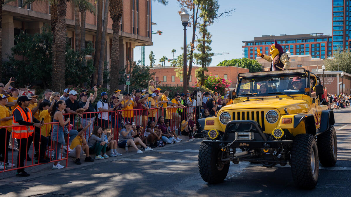 Sparky waving from a yellow jeep driving in the Homecoming parade