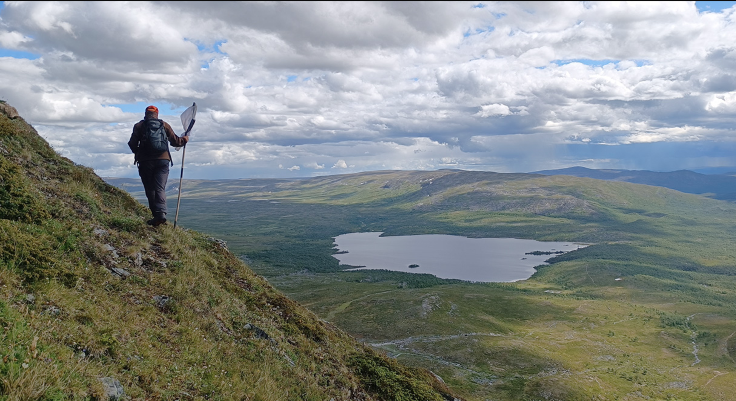 Man standing on top of a mountain while looking down at a lake