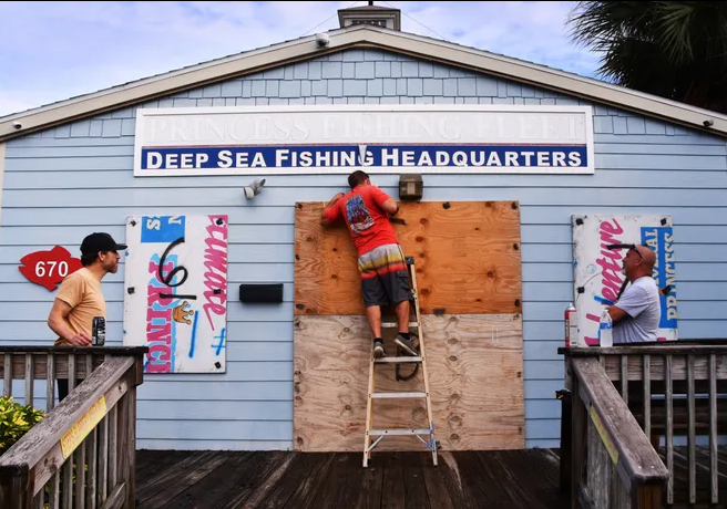 A man boarding up a window, while two other watch.