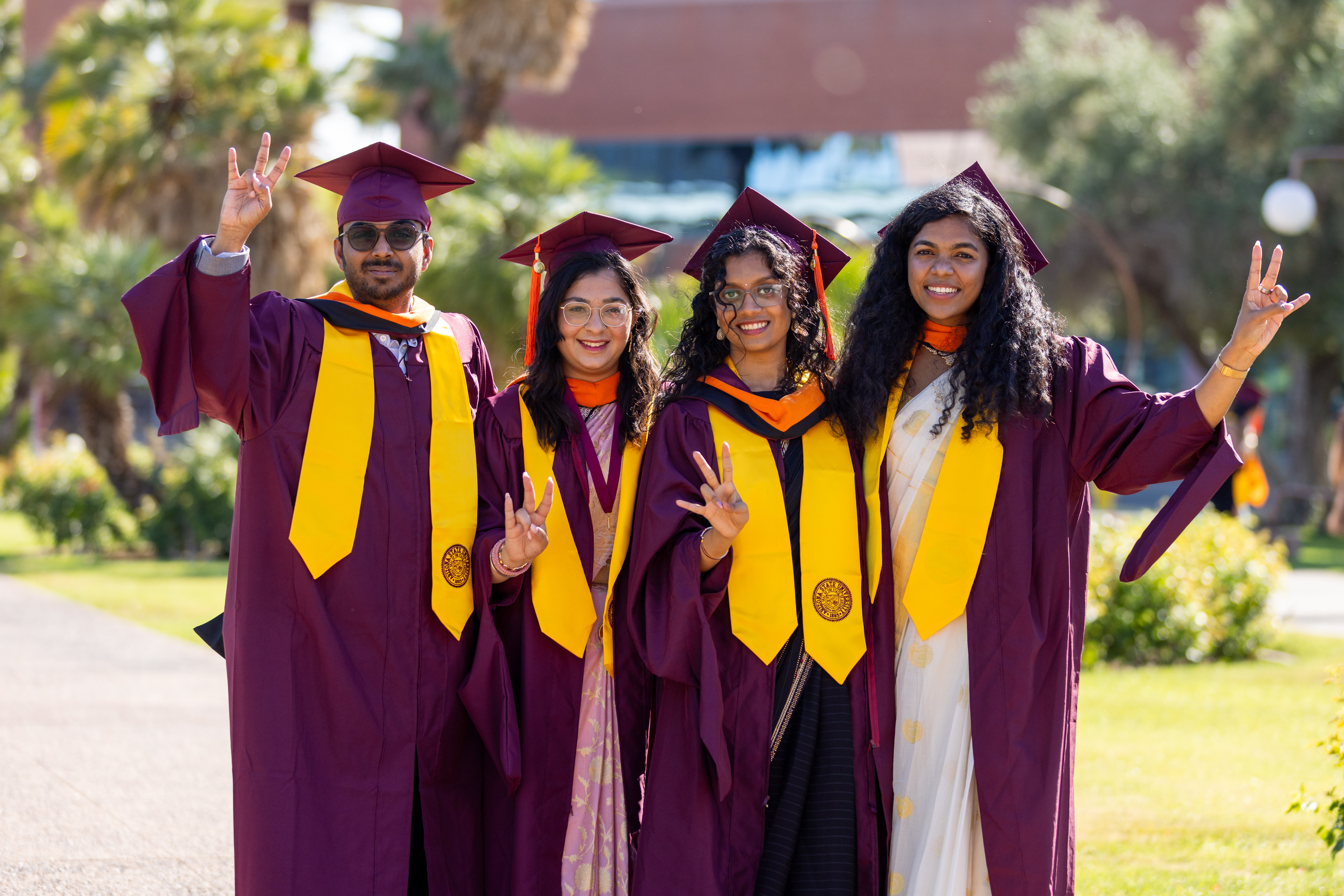 Four ASU students wearing their graduation cap and gowns.