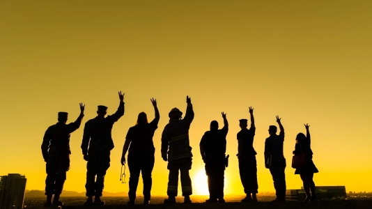Military service members standing on a hill looking toward a sunset